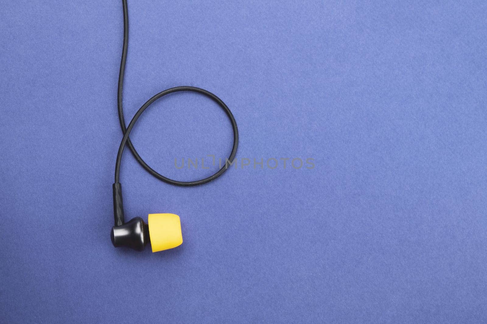 Earphone with yellow ear cushion on a blue background. in-ear headphones. audio equipment. copy space
