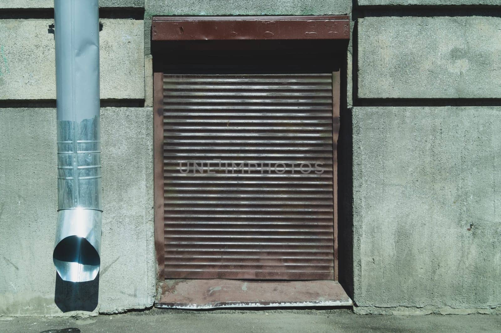 Corrugated iron blind on a concrete wall. drain pipe. metal curtain. closed window