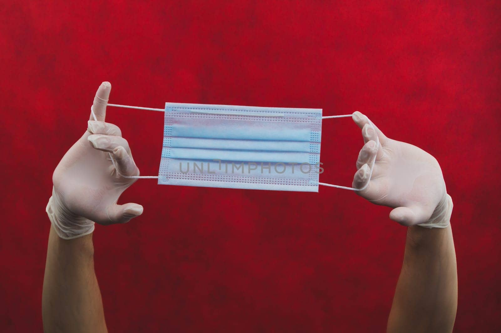Hands in protective gloves stretch a medical mask on a red background. preventive measures against respiratory illness and virus. hands in white surgical gloves holds disposable mask for protection