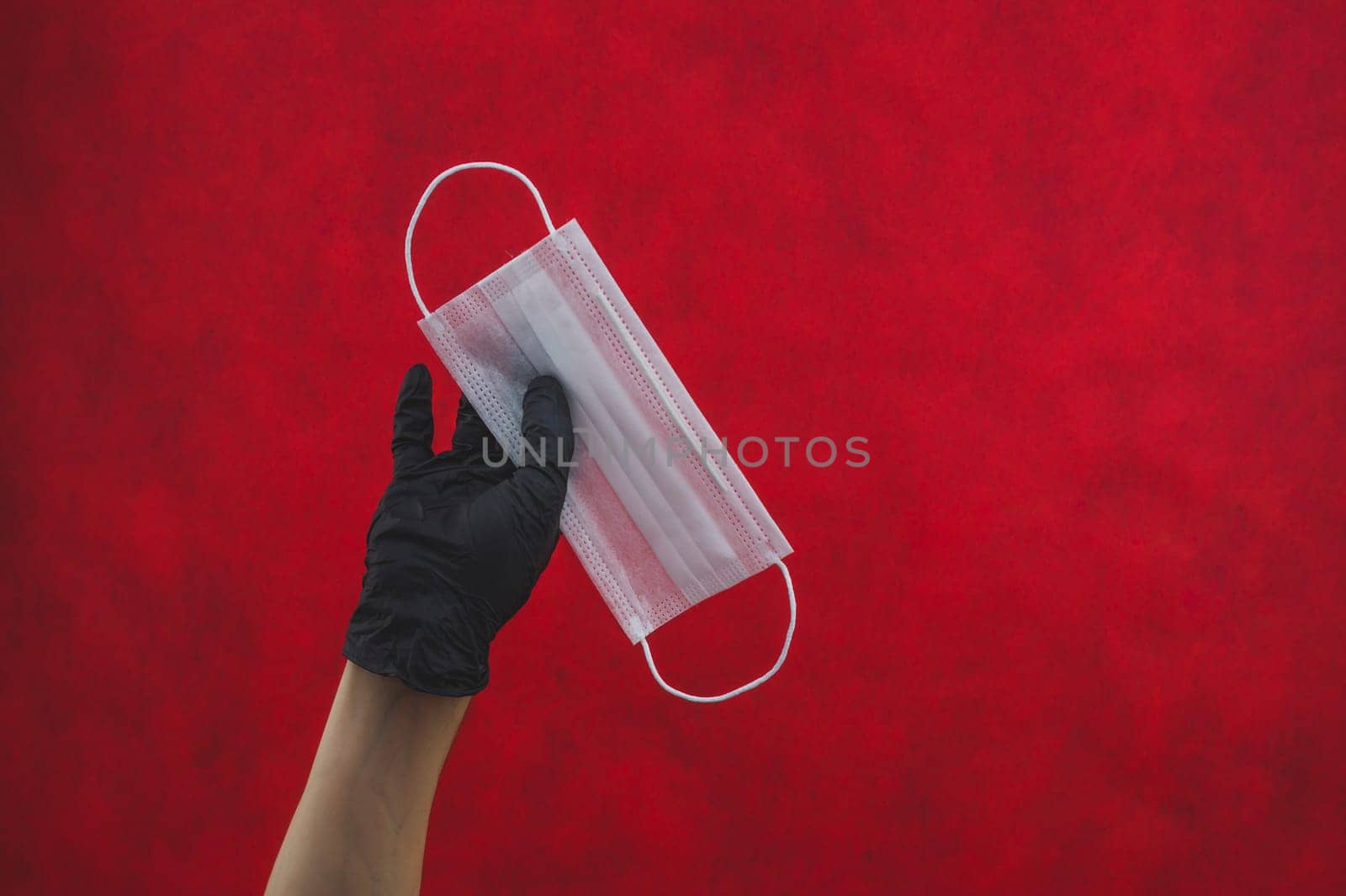 Hand in black surgical glove holds white medical mask on a red background. preventive measures against respiratory illness and virus. disposable mask for protection