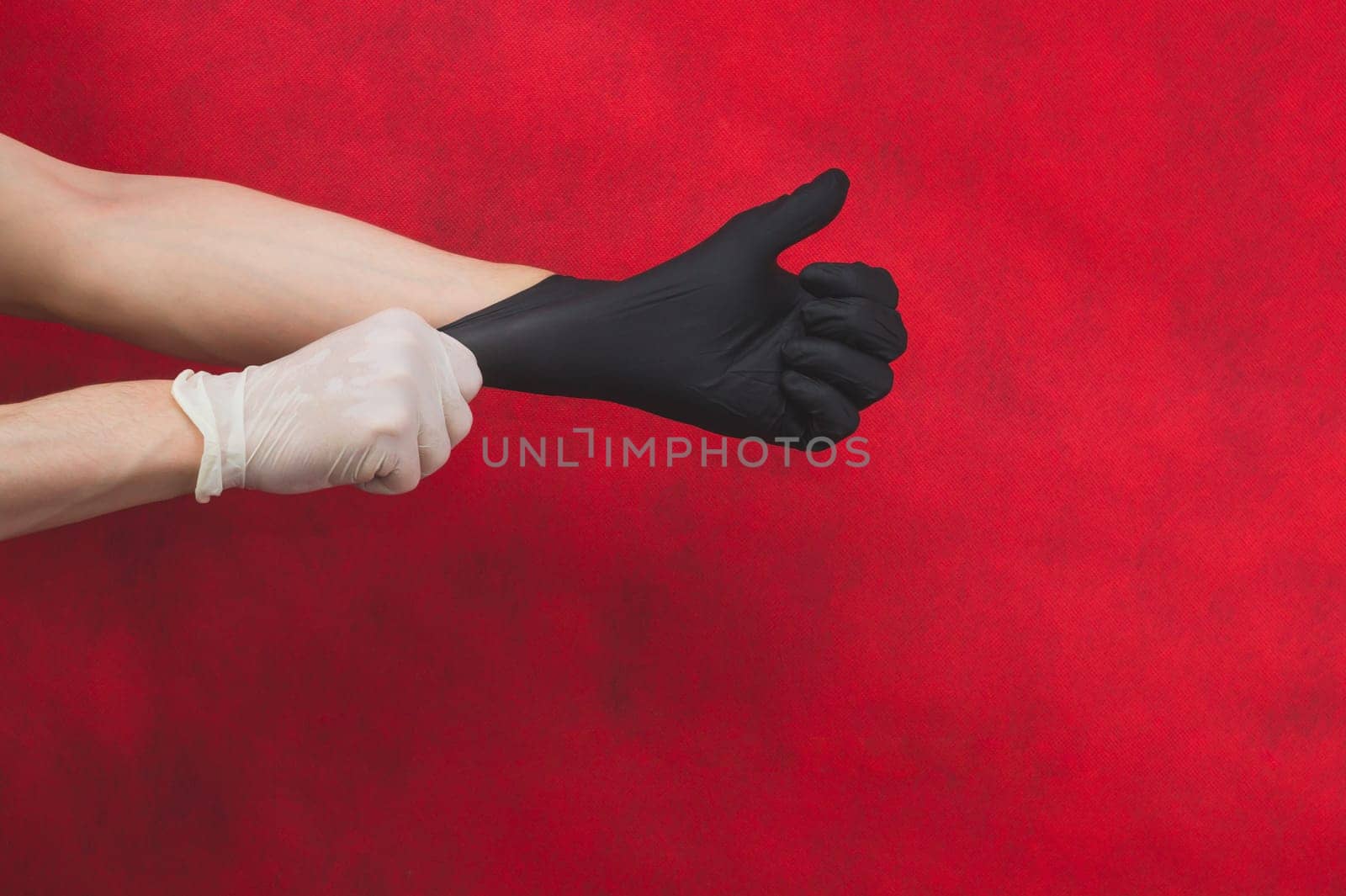 Hand in the white glove puts the black glove on the other. person puts on protective gloves on a red background