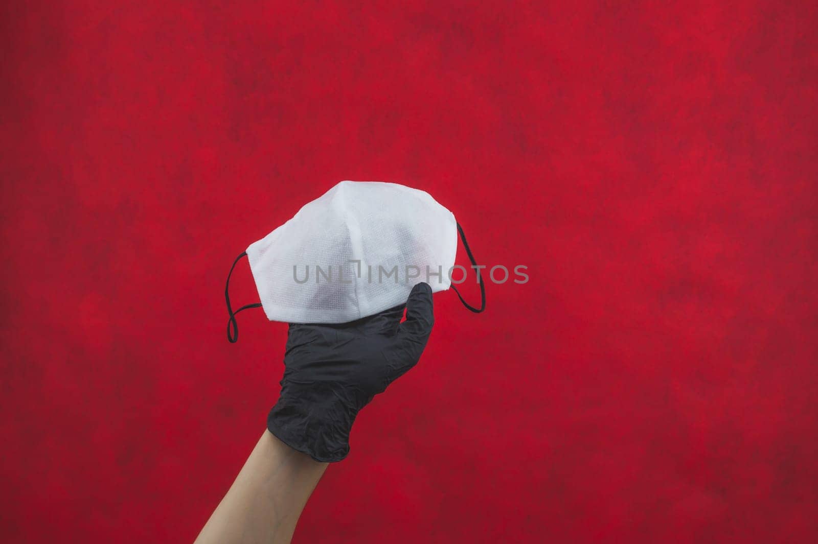 Hand in black surgical glove holds white medical mask on a red background. preventive measures against respiratory illness and virus. disposable masks for protection