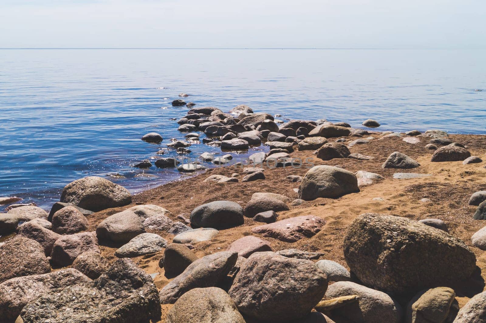 Path to the sea with stones on the sandy shore. summer landscape. horizon line