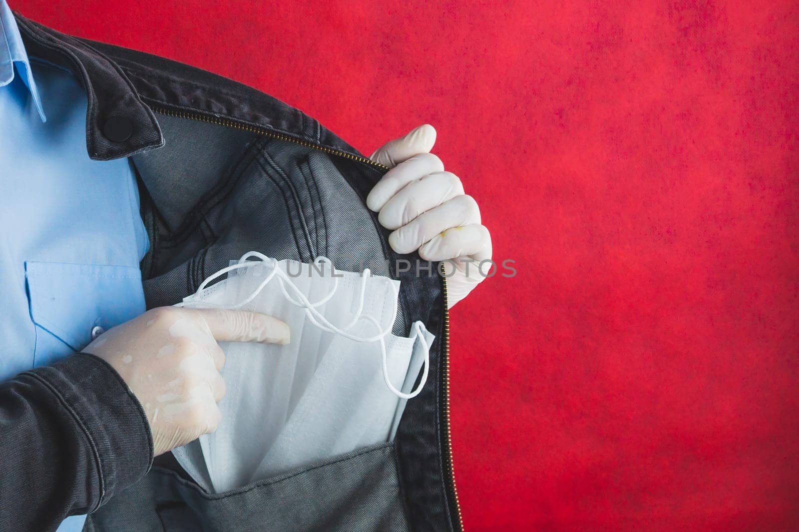 Man shows the protective masks in the pocket of jeans jacket. blue shirt. copy space. red background