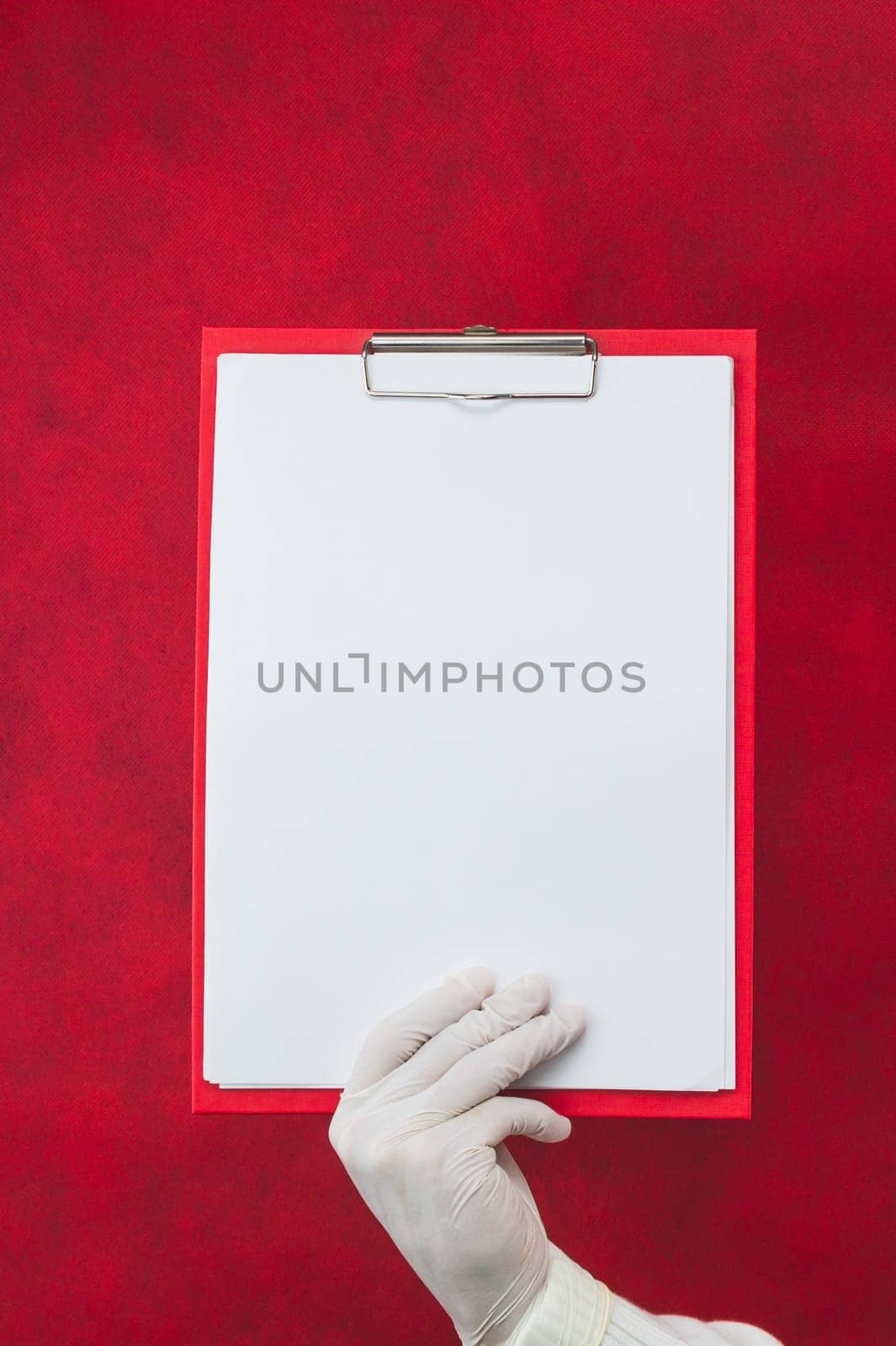 Hand in surgical glove holding white blank paper sheet on red background. template mock up. surface of leaflet. copy space