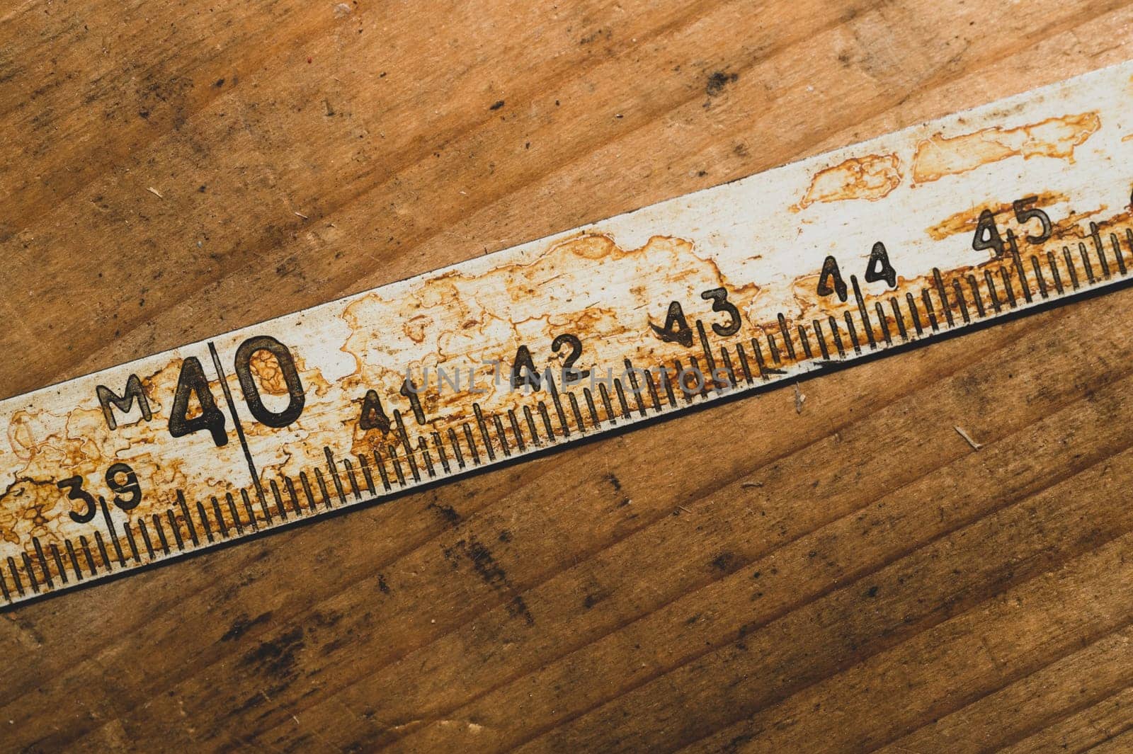 Old rusty ruler with black numbers on a working wooden table. vintage measuring tape. industrial background. carpentry workbench with copy space