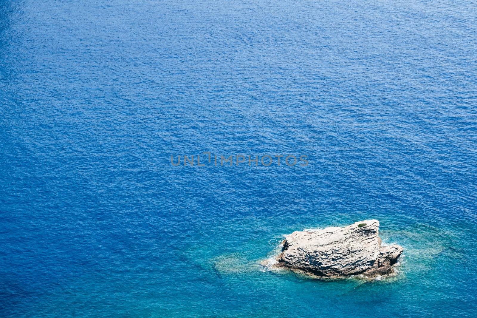 closeup top view of lonely rock surrounded by azure blue sea