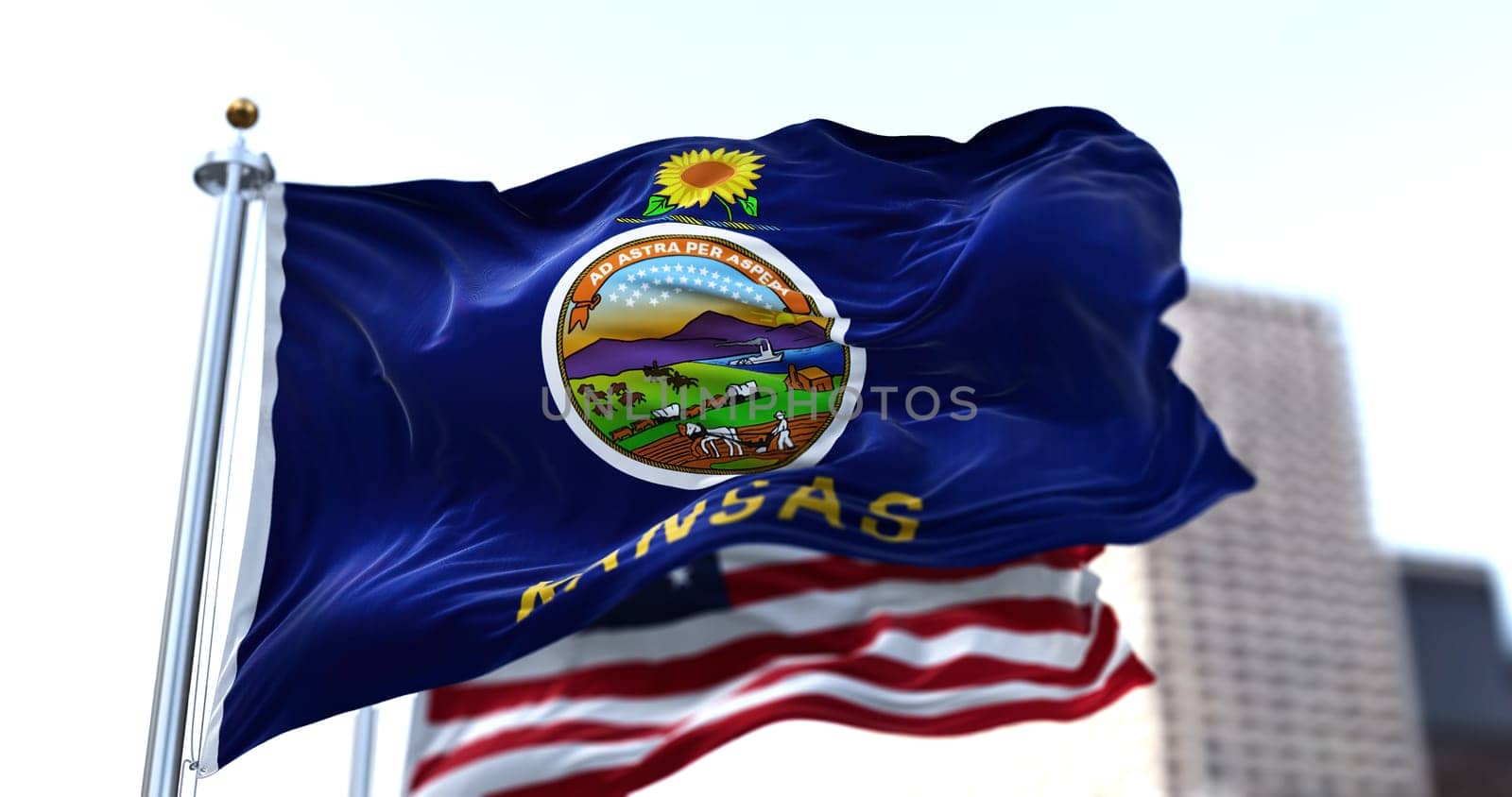 the flag of the US state of Kansas waving in the wind with the American stars and stripes flag blurred in the background. Seal of Kansas on a blue field and a sunflower above the seal