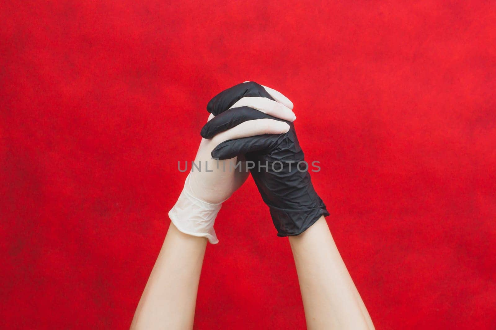 Fingers locked together. hands in protective gloves clasped each other. one hand in black glove, other in white. gesturing hands in medical gloves on a red background