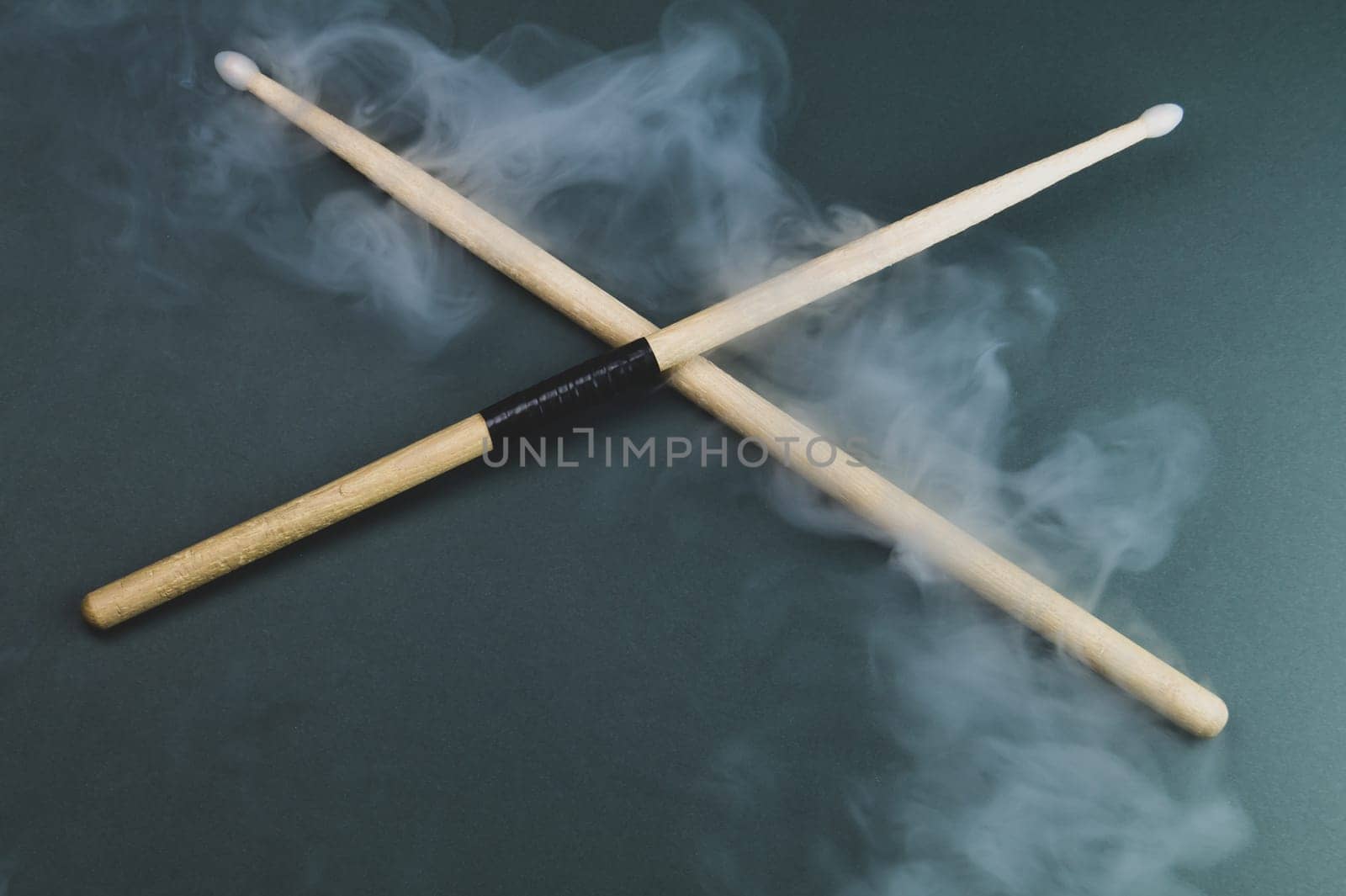A pair of wooden drumsticks in the smoke on color background. copy space