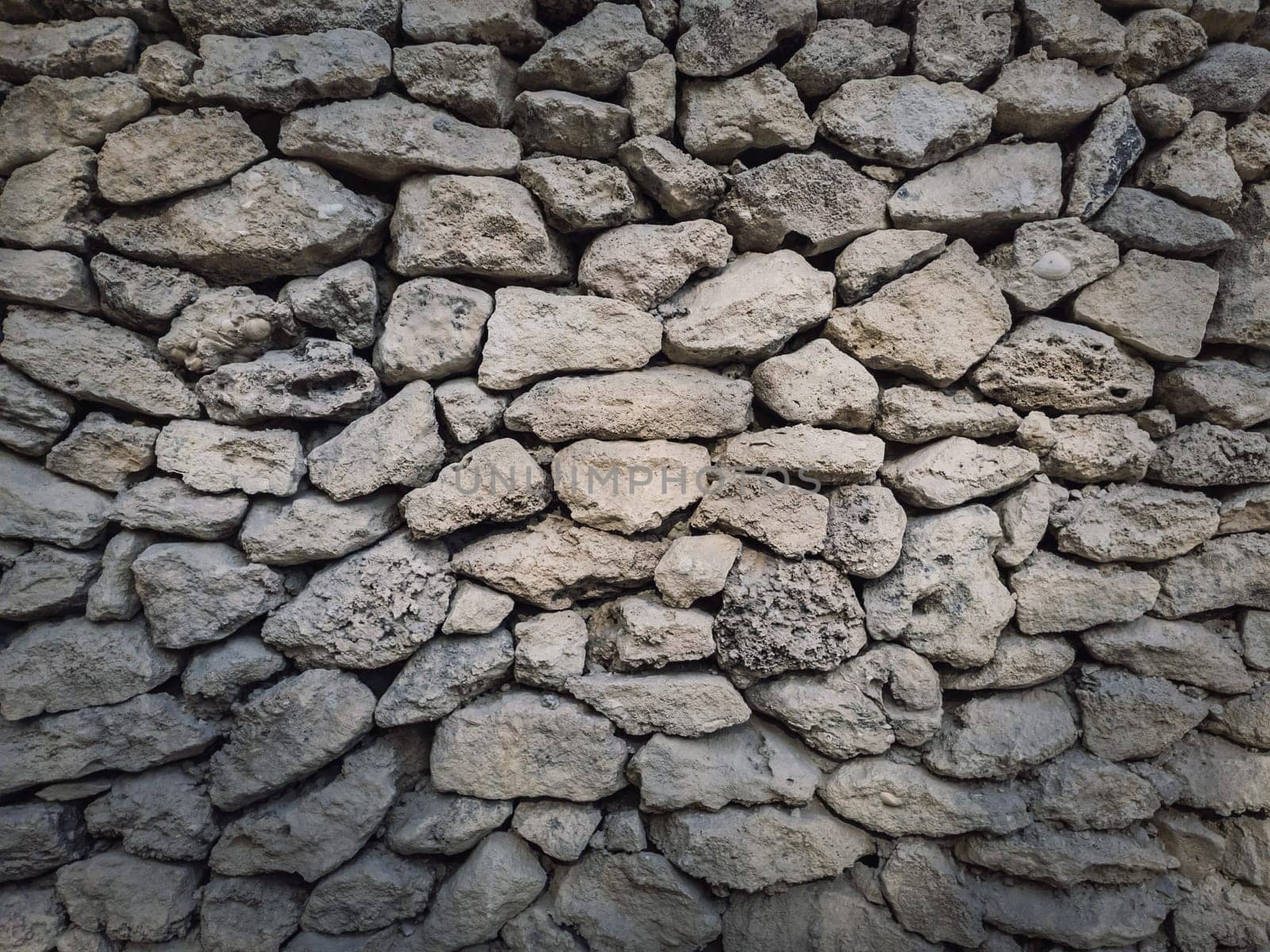 Irregular stone masonry wall background. Old limestone rocks of different size and shapes stacked carefully. Detailed texture of construction element. Antique rough manual work.