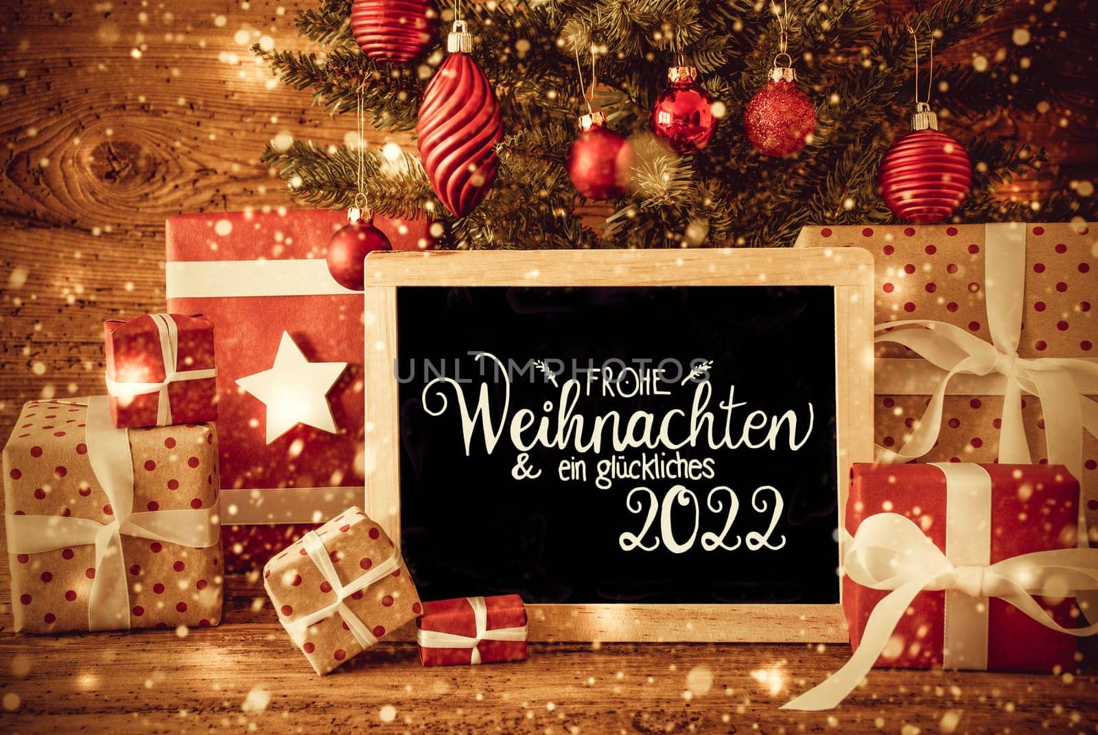 Blackboard With German Text Frohe Weihnachten Und Ein Glueckliches 2022 Means Merry Christmas And A Happy 2022. Christmas Tree With Decoration Like Ball, Gifts And Presents, Snowflakes