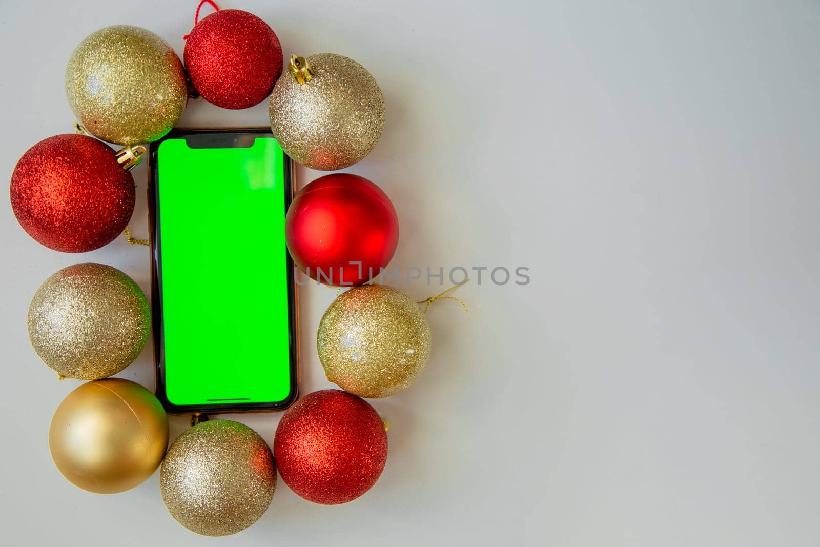 A phone with a green screen lies among the golden and red Christmas balls. High quality photo