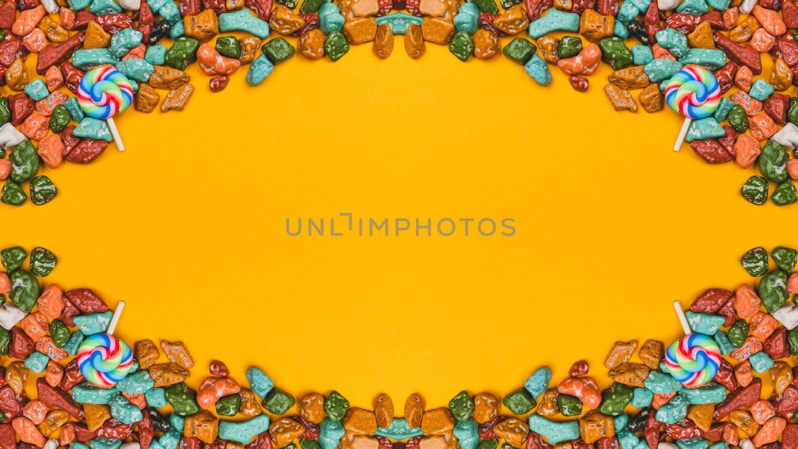 Lollipops and candy pebbles on a yellow background. sweets in the form of colored stones. symmetrical frame made from colorful candies. festive decoration