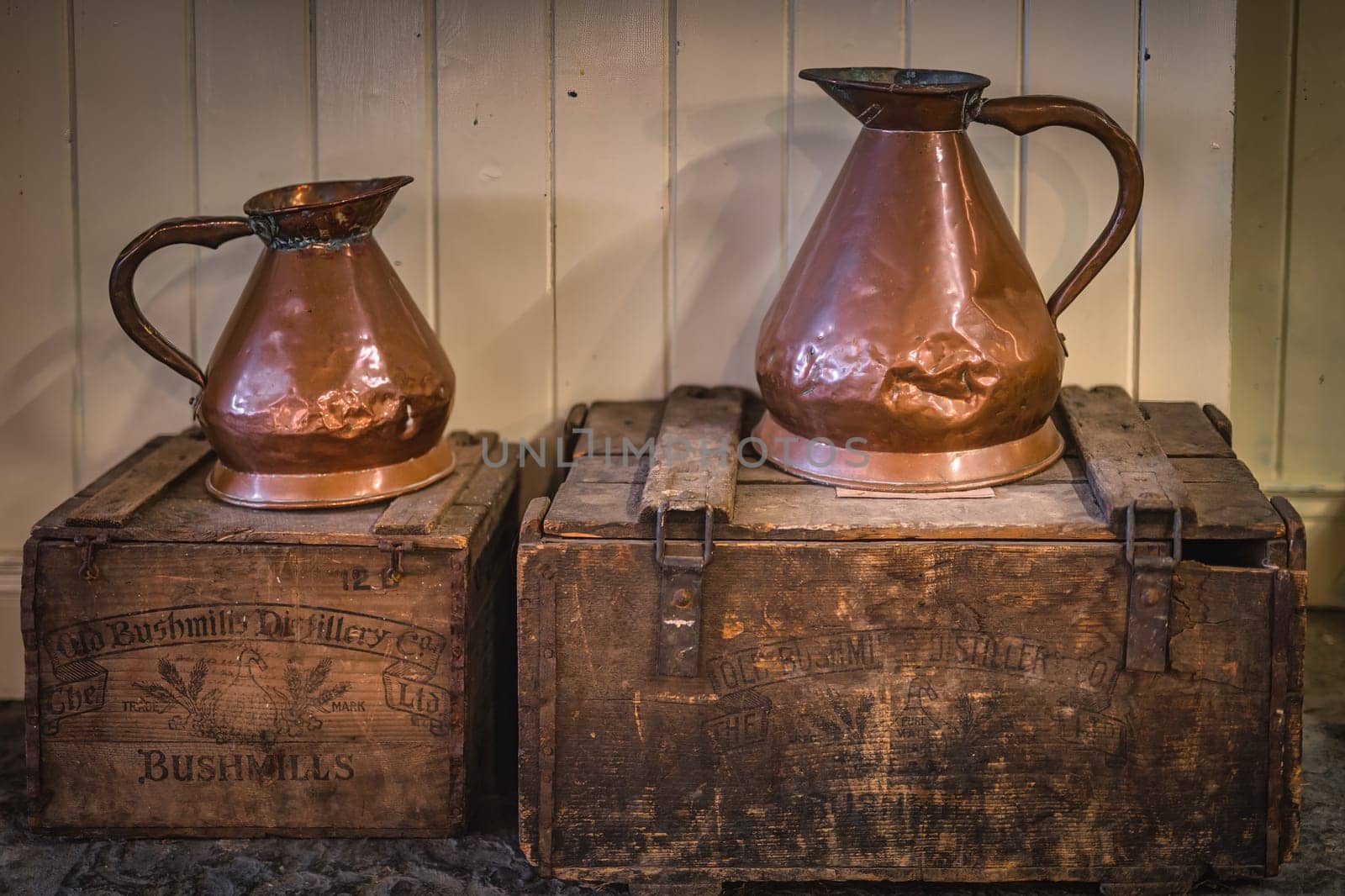 Bushmills, Northern Ireland, Aug 2019 Vintage battered copper jugs standing on wooden crates with Bushmills whiskey bandings