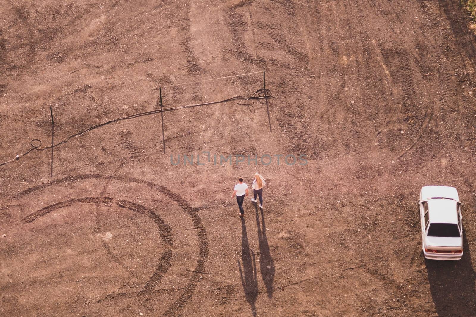 Couple walking on the sand near a car. aerial view. ground with tracks and footprints. view from above of a couple of tourists. conceptual background with copy space