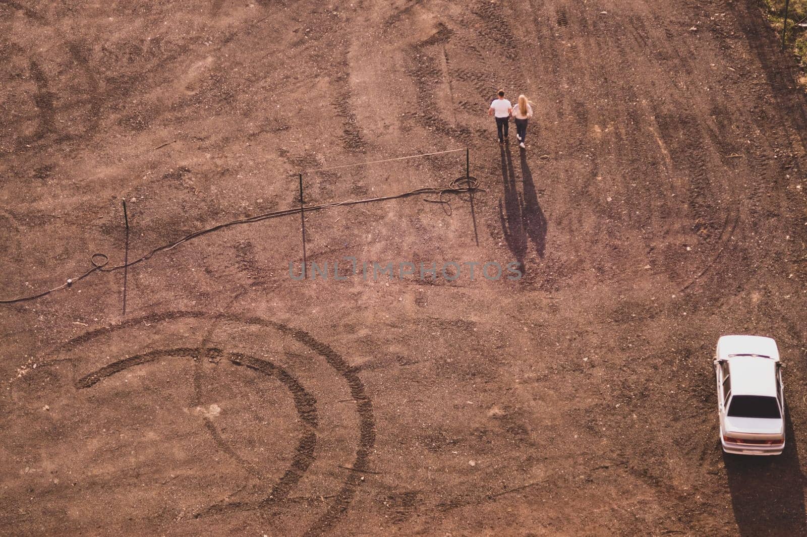 Couple walking on the sand near a car. aerial view. ground with tracks and footprints. view from above of a couple of tourists. conceptual background with copy space