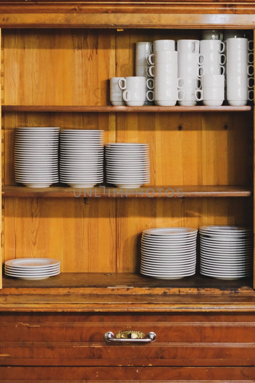 Vintage cupboard with white dinnerware. old wooden kitchen cabinet with stack of white plates and cups. retro sideboard