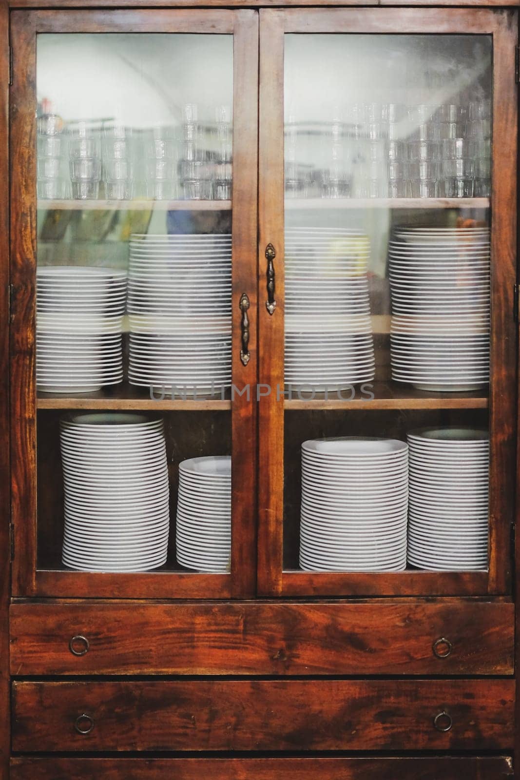 Vintage cupboard with white dinnerware. old wooden kitchen cabinet with stack of white plates and cups. retro sideboard
