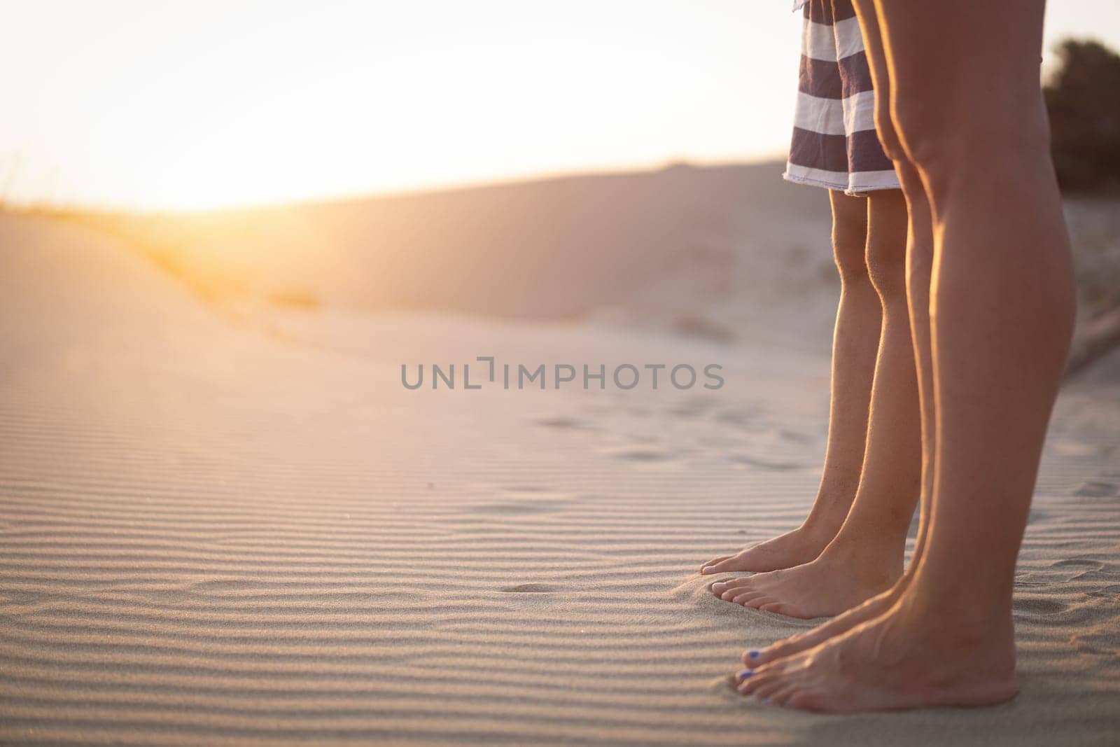 side view closeup of young woman and her child feet standing on sand dunes at sunrise