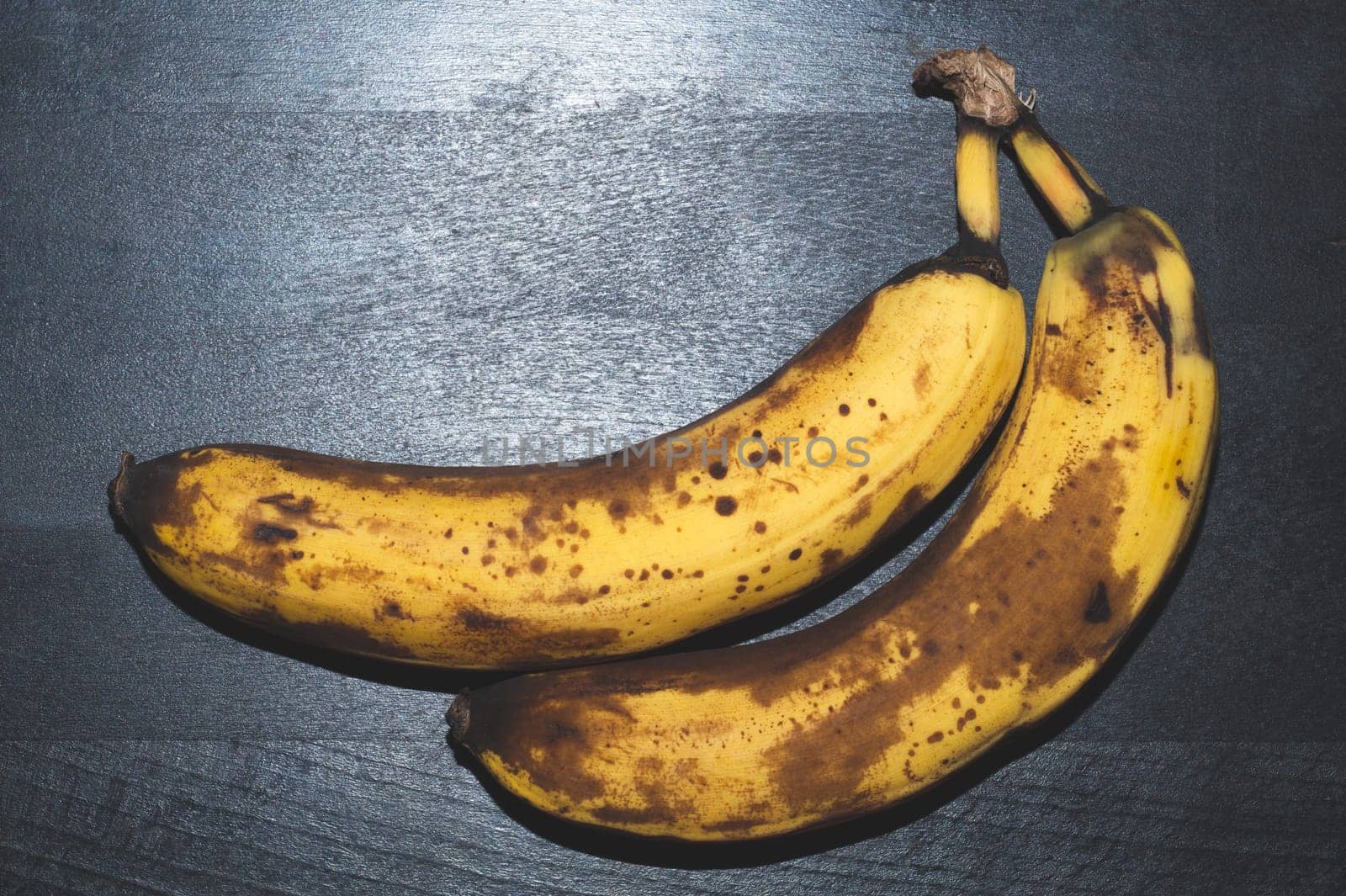 Overripe bananas with spots. fruits lays on black wooden table