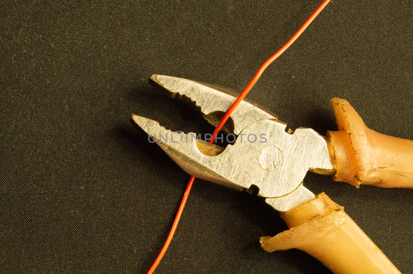 Pliers cuts a red wire on black background. pliers with orange handles. work tool. copy space