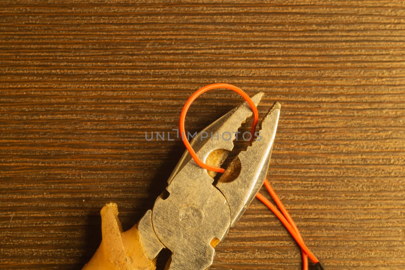 Pliers cuts a red wire on wooden background. pliers with orange handles. work tool. copy space