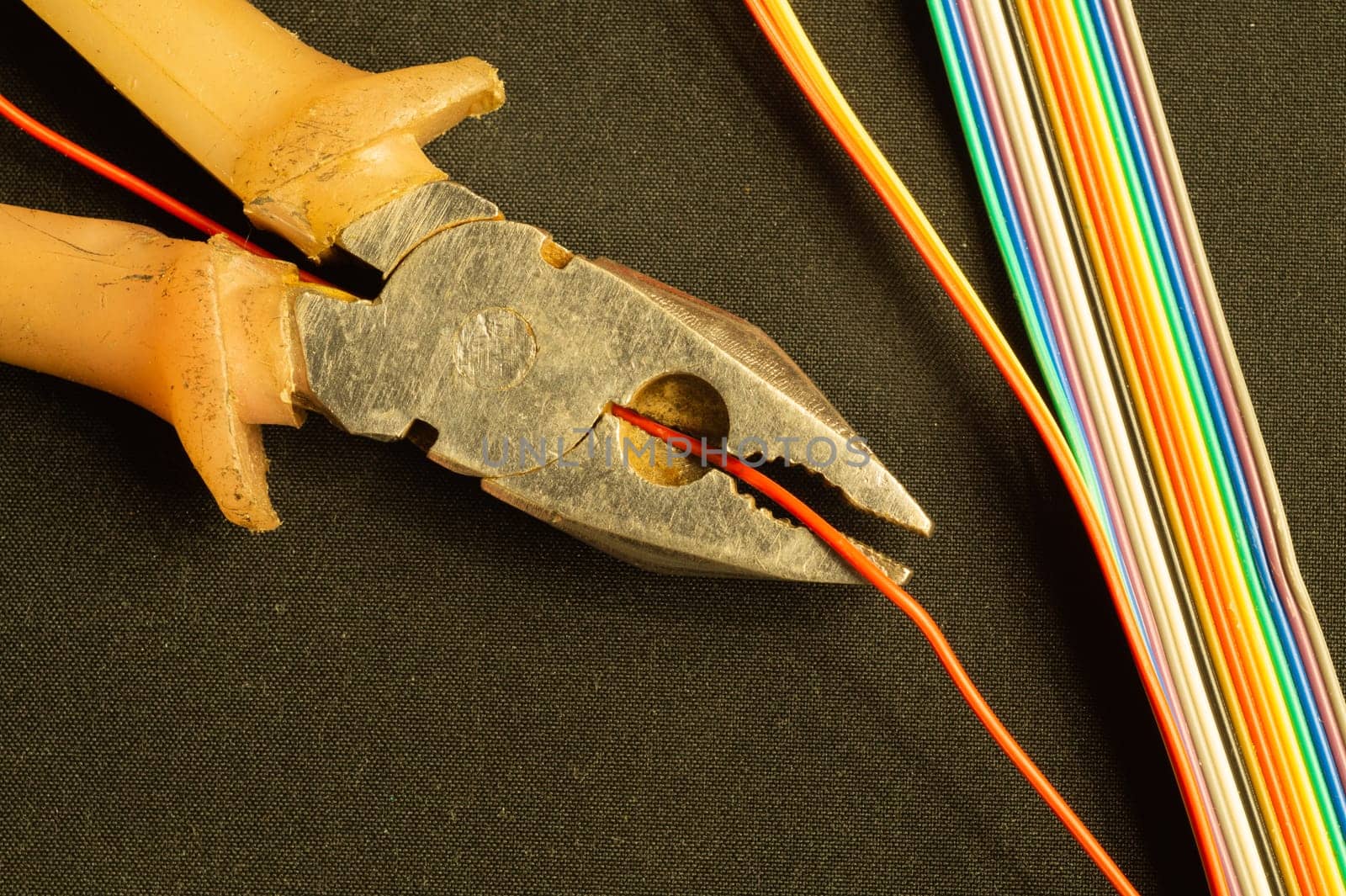 Pliers cuts a red wire on black background. pliers with orange handles and colorful wires. work tool. copy space