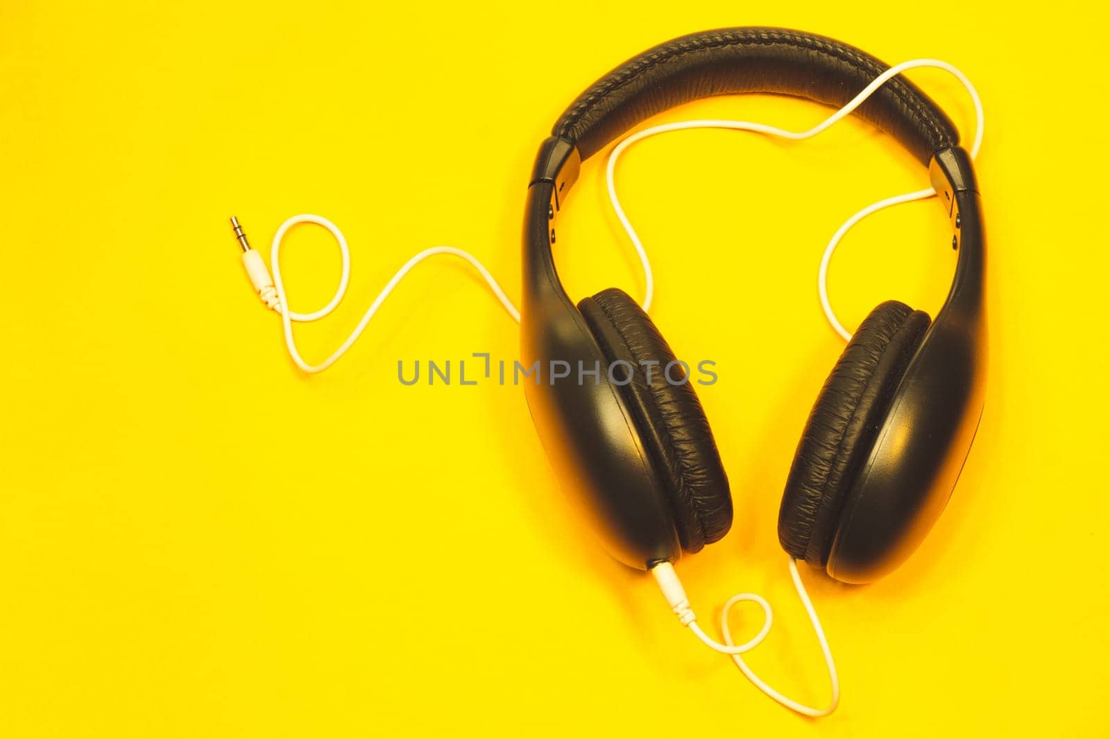 Black headphones with white cable on a yellow background. modern earphones