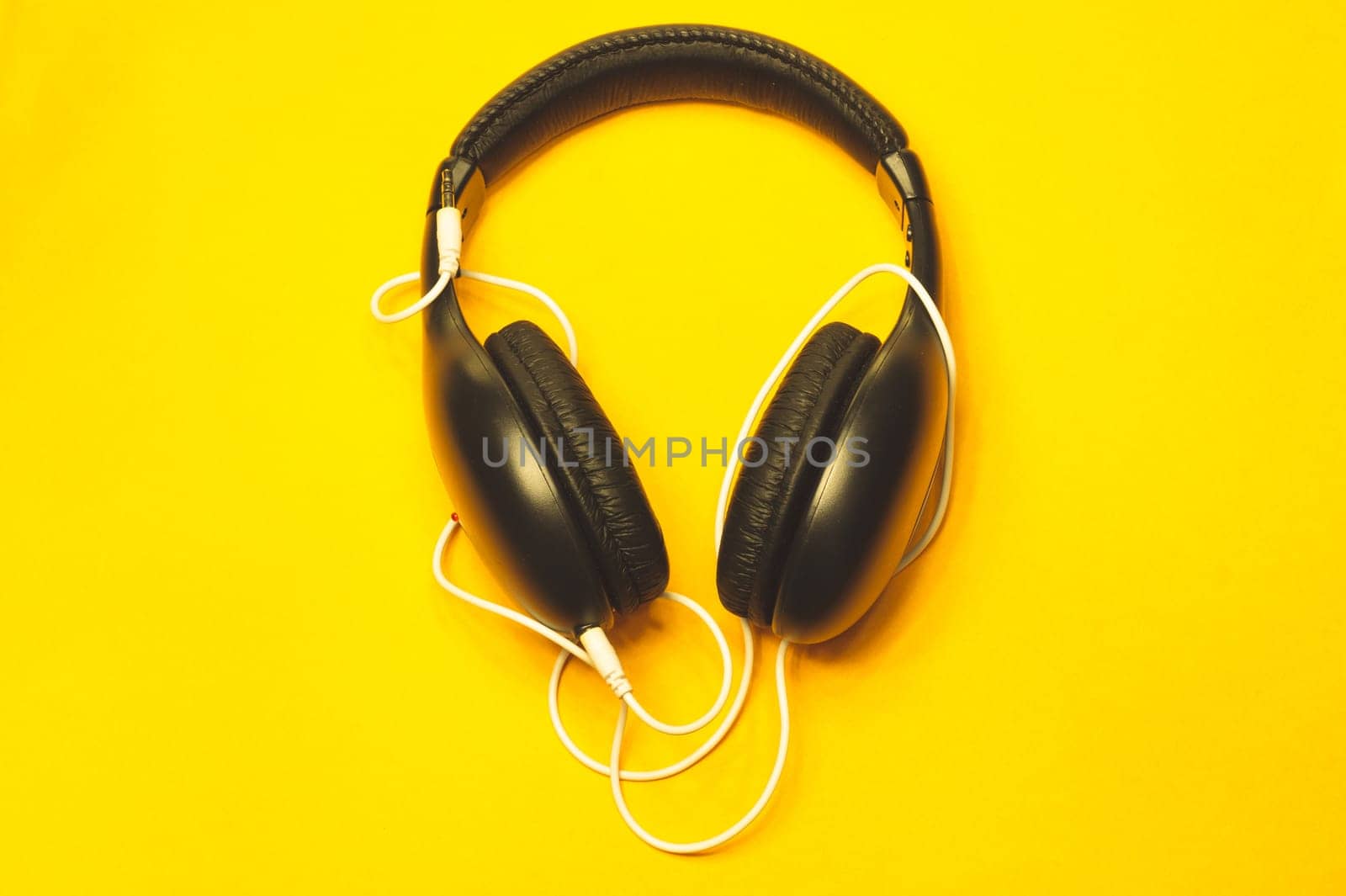 Black headphones with white cable on a yellow background. modern earphones