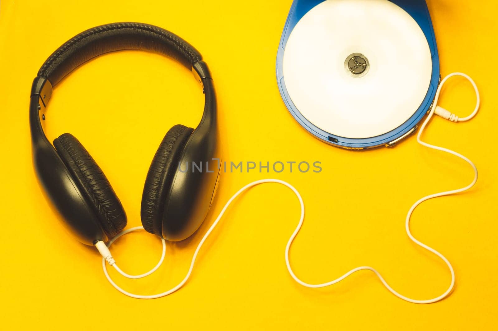 Black headphones with a white cable on a yellow background. compact disc player with white cd and earphones