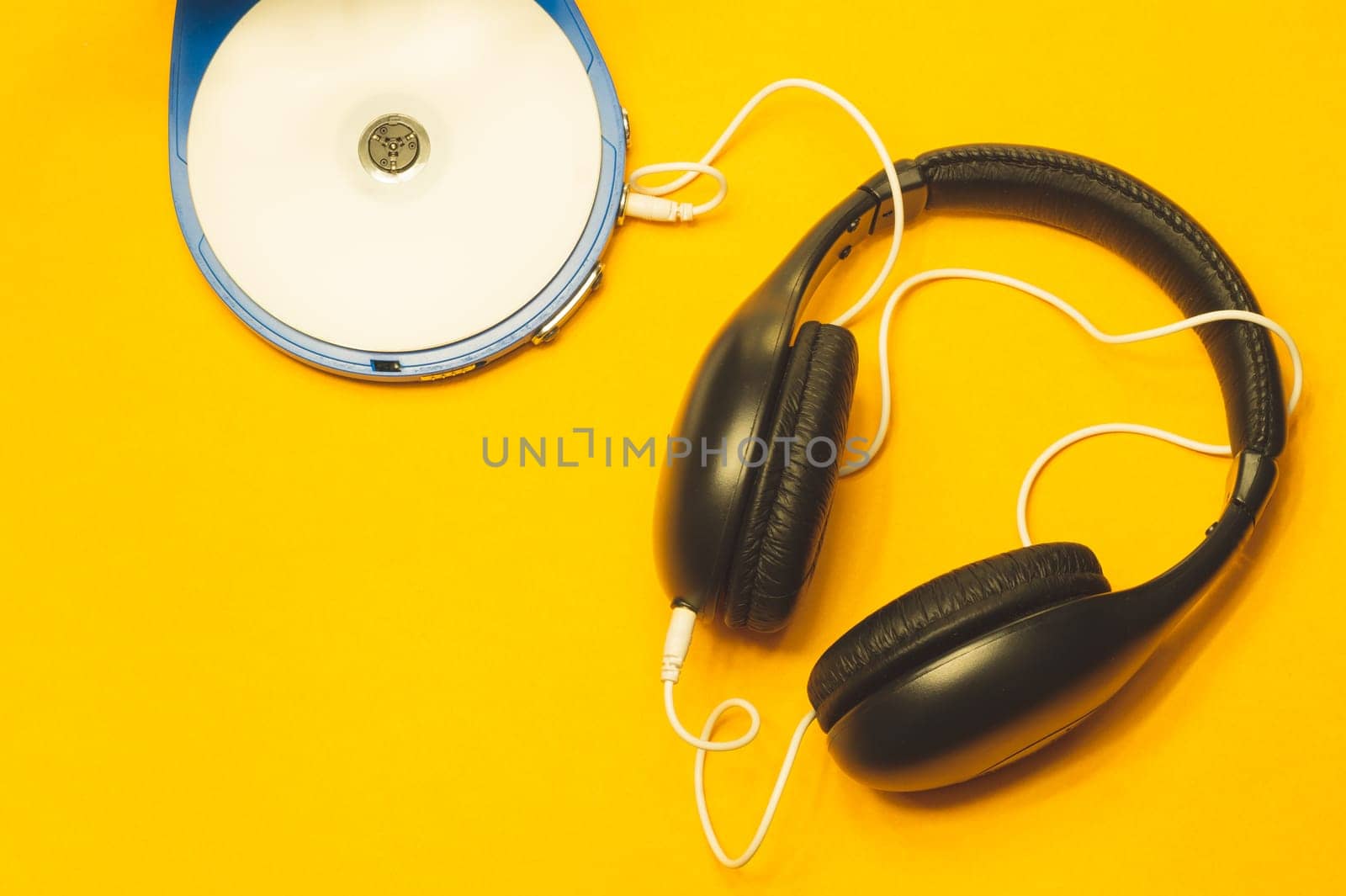Black headphones with a white cable on a yellow background. compact disc player with white cd and earphones