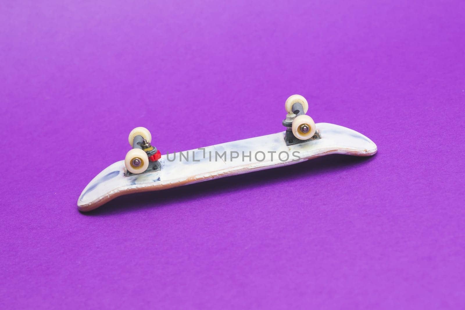 Small skateboard on purple background. tiny skate for fingers. fingerboard close up. copy space