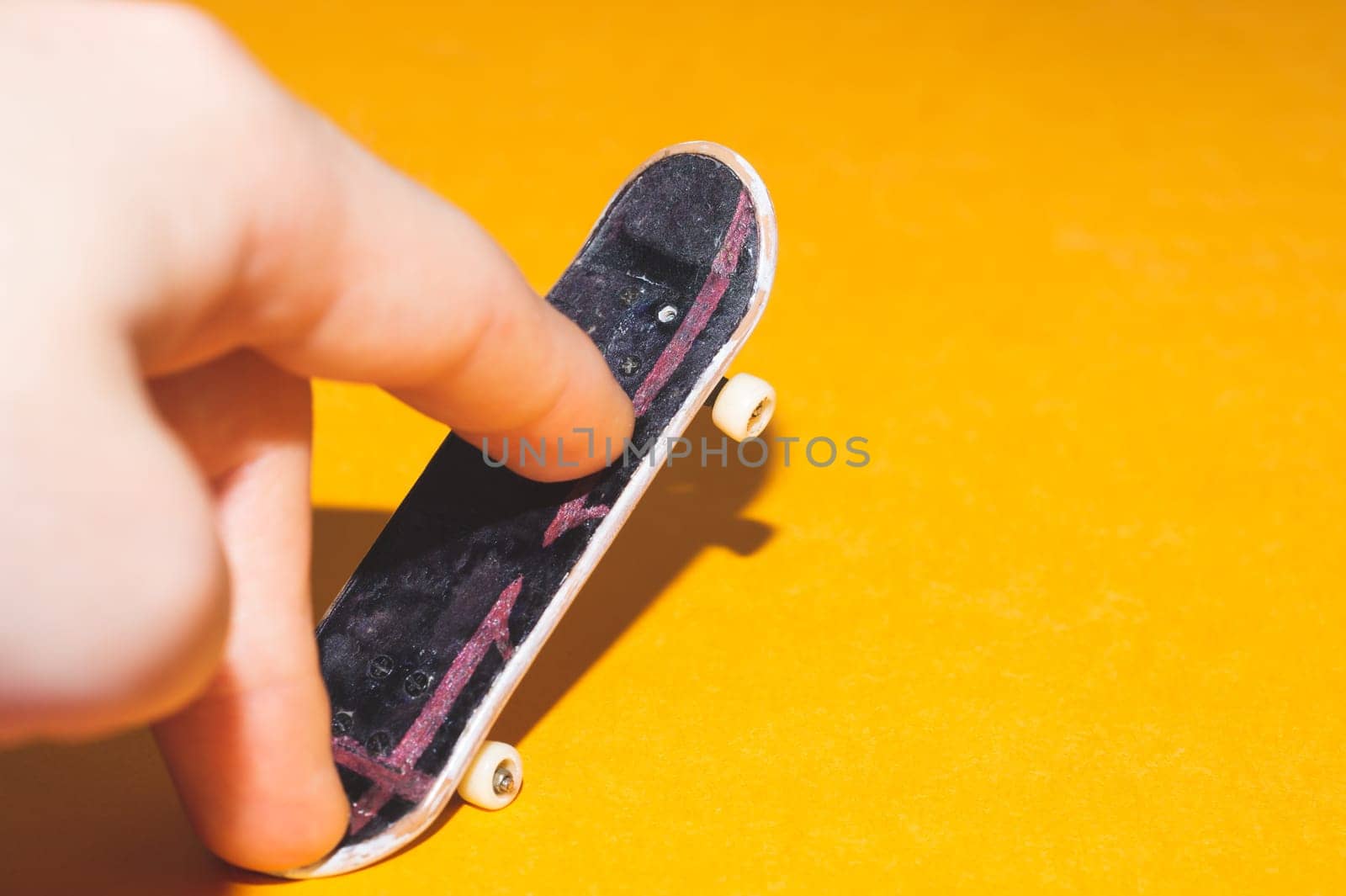 Small skateboard on yellow background. fingers on tiny skate. playing with fingerboard. home leisure concept. copy space