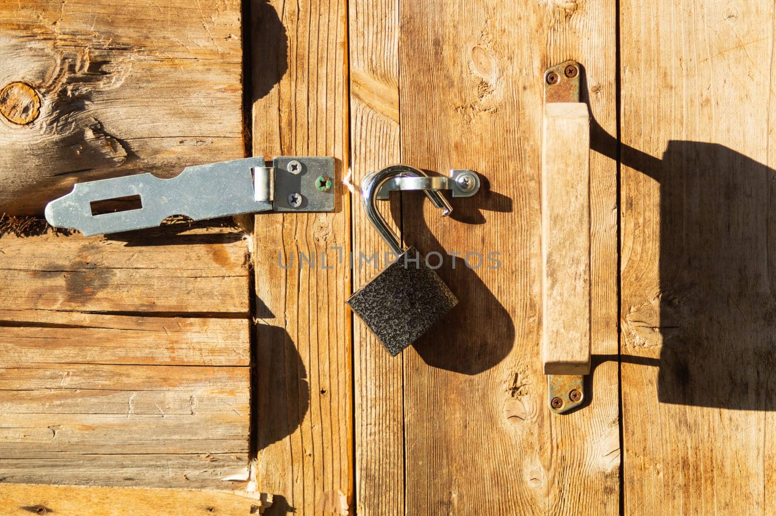Metal padlock on a wooden door with opened latch