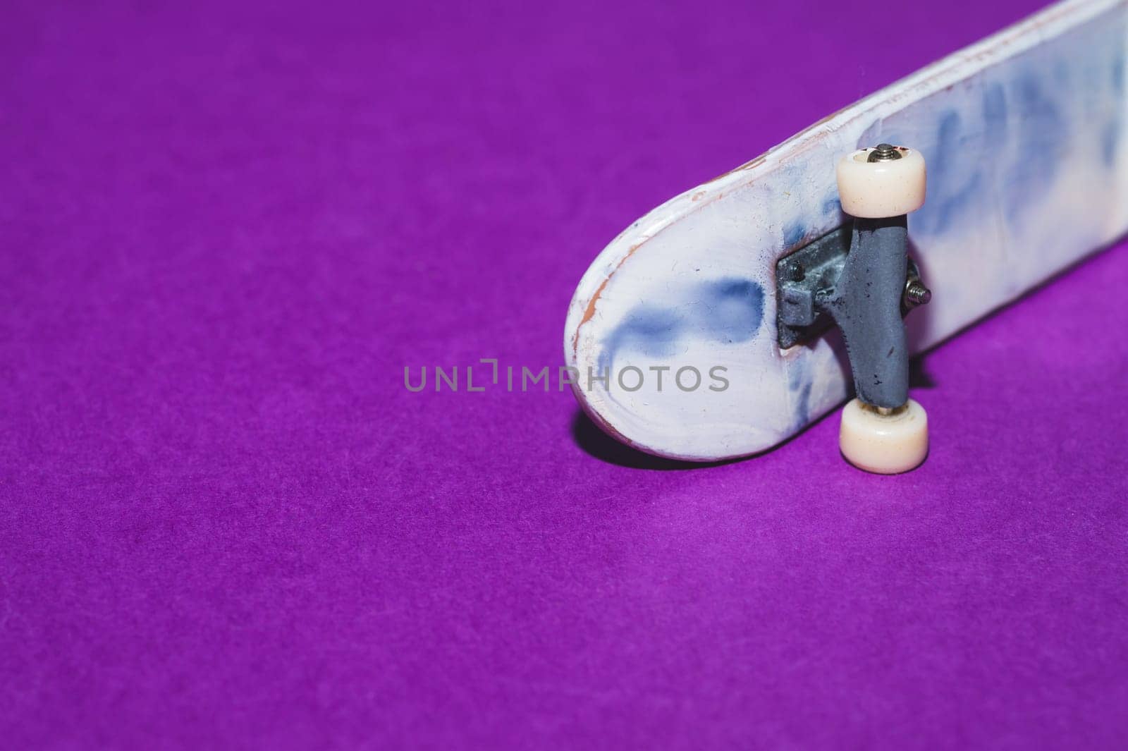 Small skateboard on purple background. tiny skate for fingers. fingerboard close up. copy space
