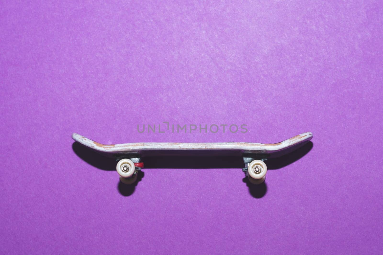 Small skateboard on purple background. tiny skate for fingers. fingerboard close up. copy space