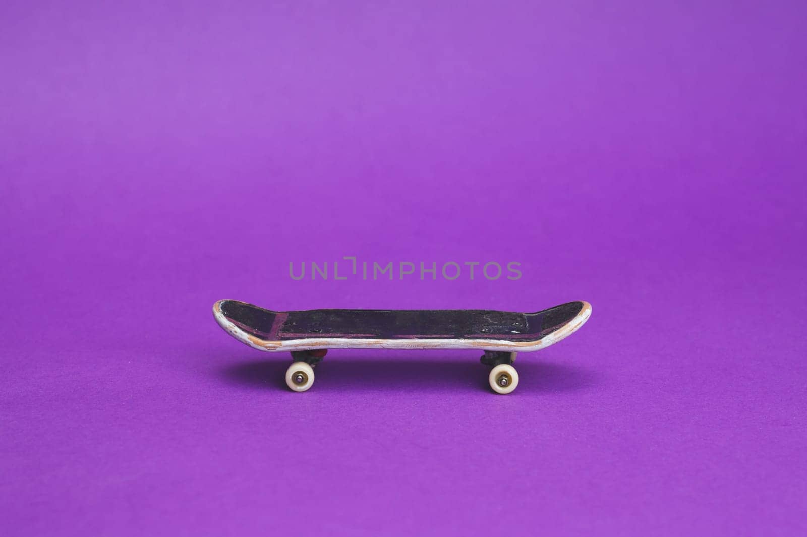 Small skateboard on purple background. tiny skate for fingers. fingerboard close up. copy space