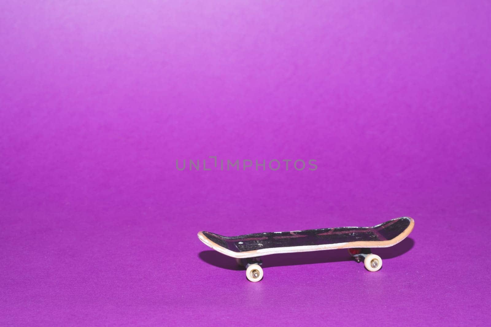 Small skateboard on purple background. tiny skate for fingers. fingerboard close up. copy space
