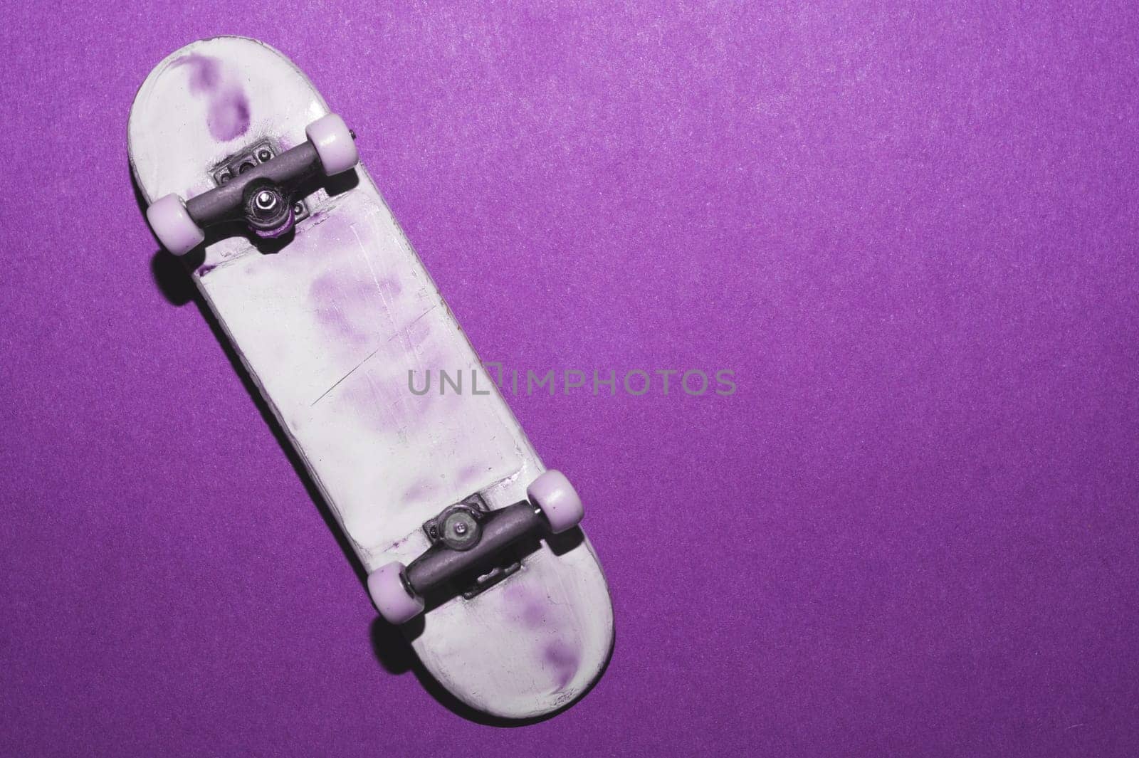 Small skateboard on purple background. tiny skate for fingers. fingerboard close up. copy space