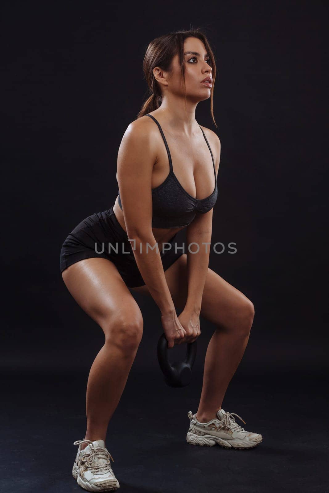 Fit young woman doing squats while lifting a kettle bell.