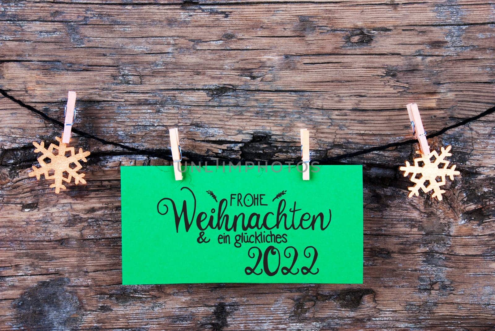 Green Label With German Calligraphy Frohe Weihnachten Und Ein Glueckliches 2022 Means Merry Christmas And Happy 2022. Rope WIth Christmas Ornamen. Rustic Wooden Background