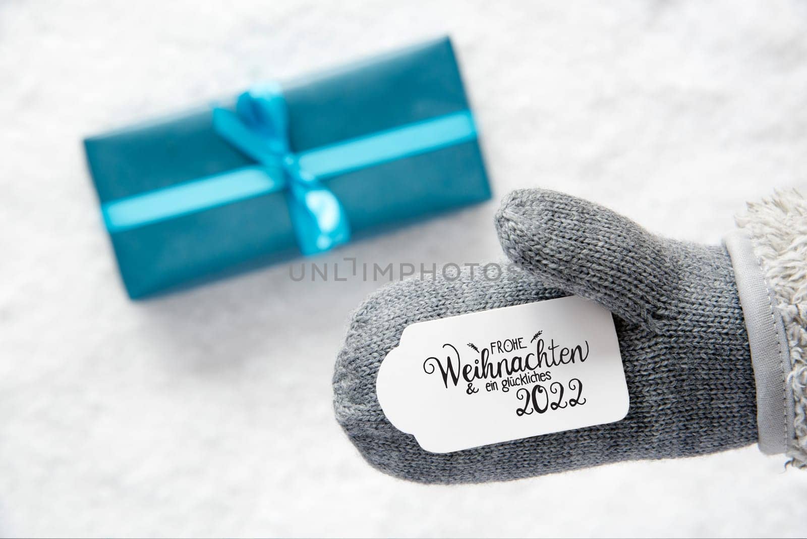 Label With German Calligraphy Frohe Weihnachten Und Ein Glueckliches 2022 Means Merry Christmas And A Happy 2022. Gray Glove With Turquoise Gift And Snow Background