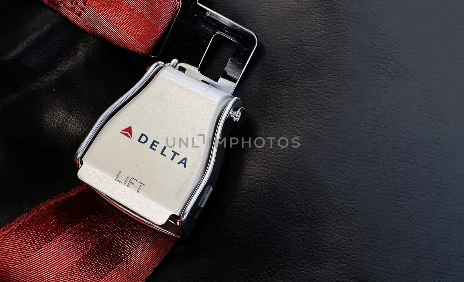 Atlanta, USA, October 2021: Red lap belt of an empty seat inside an airplane with the Delta Airlines logo printed on the metal. Delta is one of the major airlines of the United States