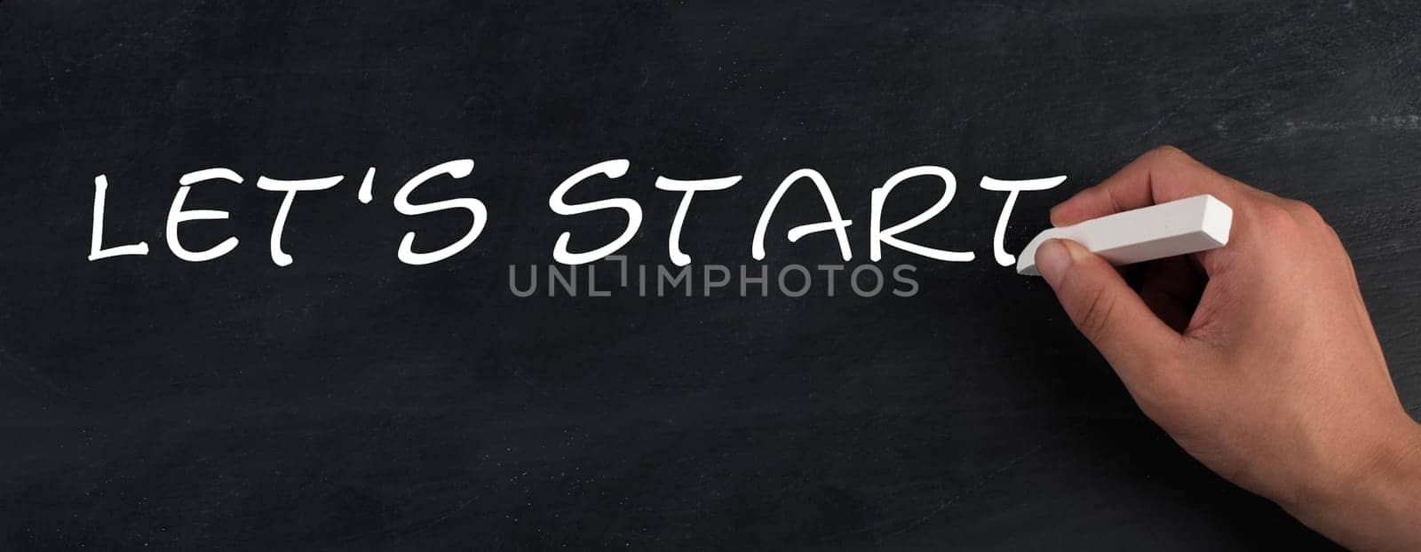 The words lets start are standing on a chalkboard, hand with chalk handwriting