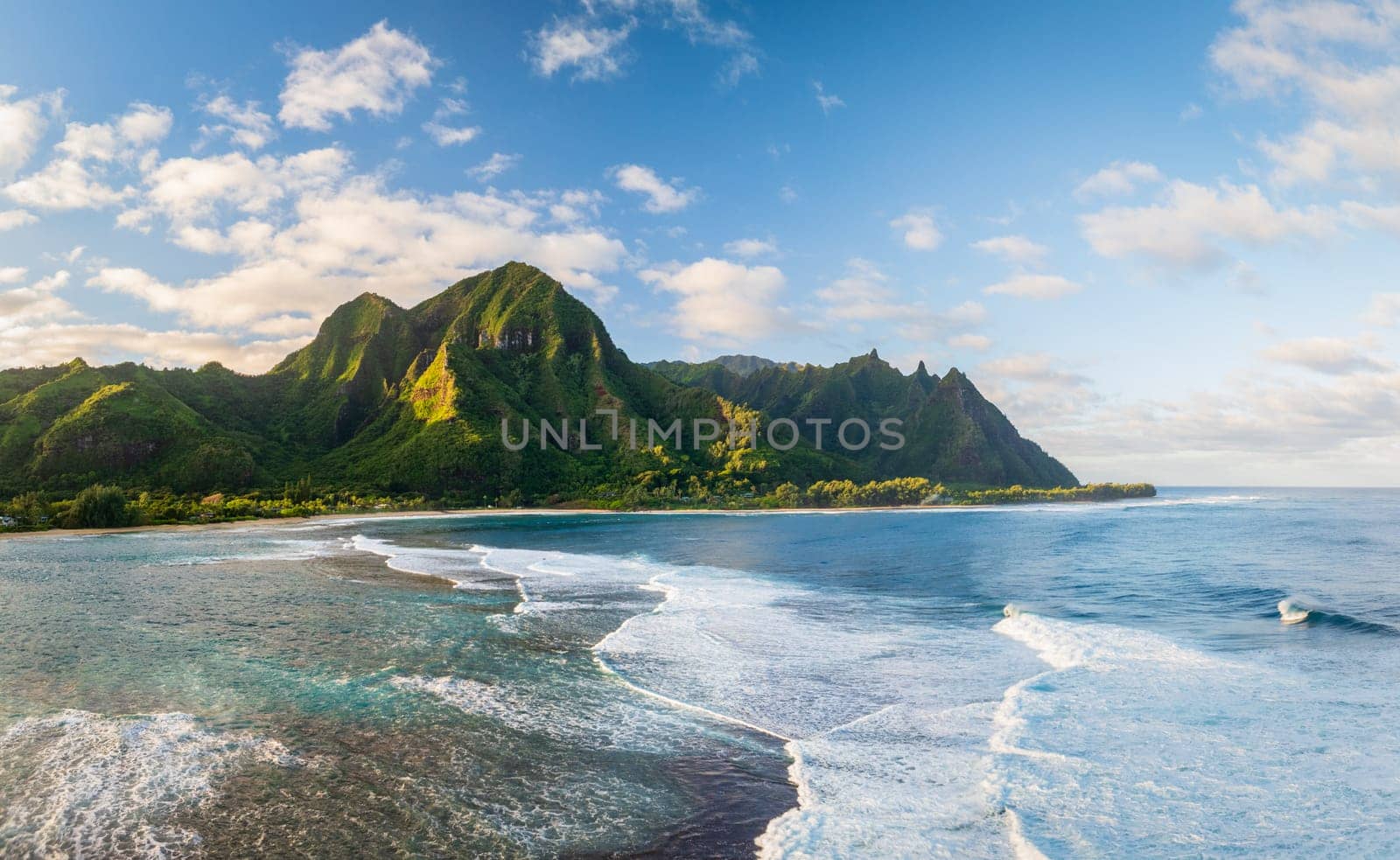 Tunnels Beach panorama view from above at sunset, with the clear turquoise water and lush green mountains in the background