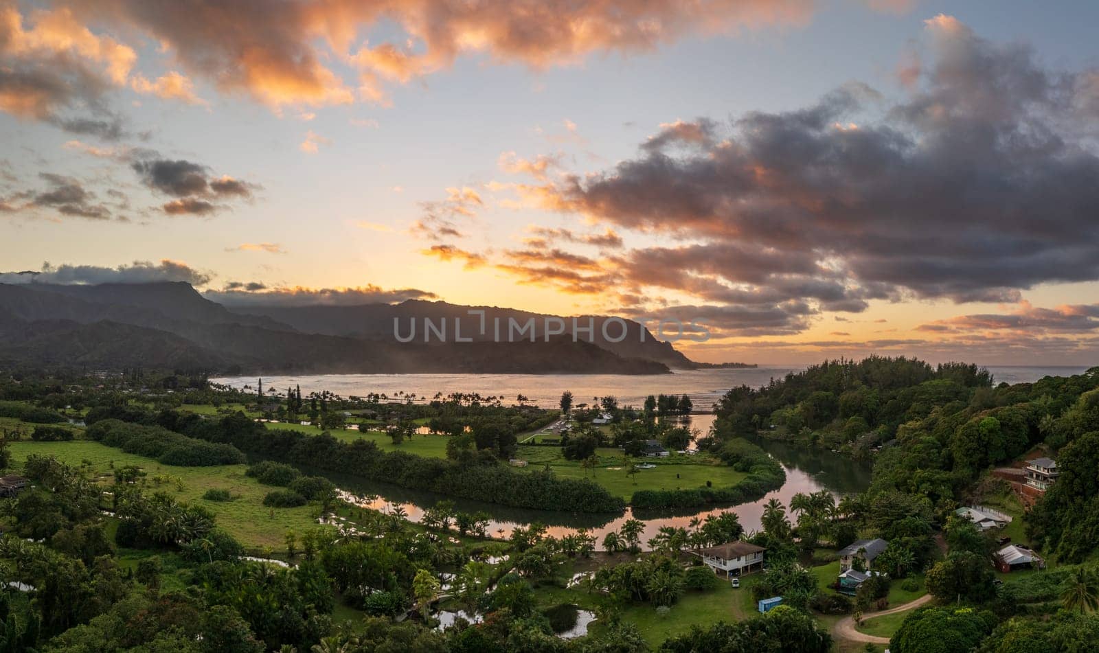 A vibrant aerial view of sunset clouds over the lush landscape of Hanalei Bay, framed by majestic mountains in Kauai, Hawaii.