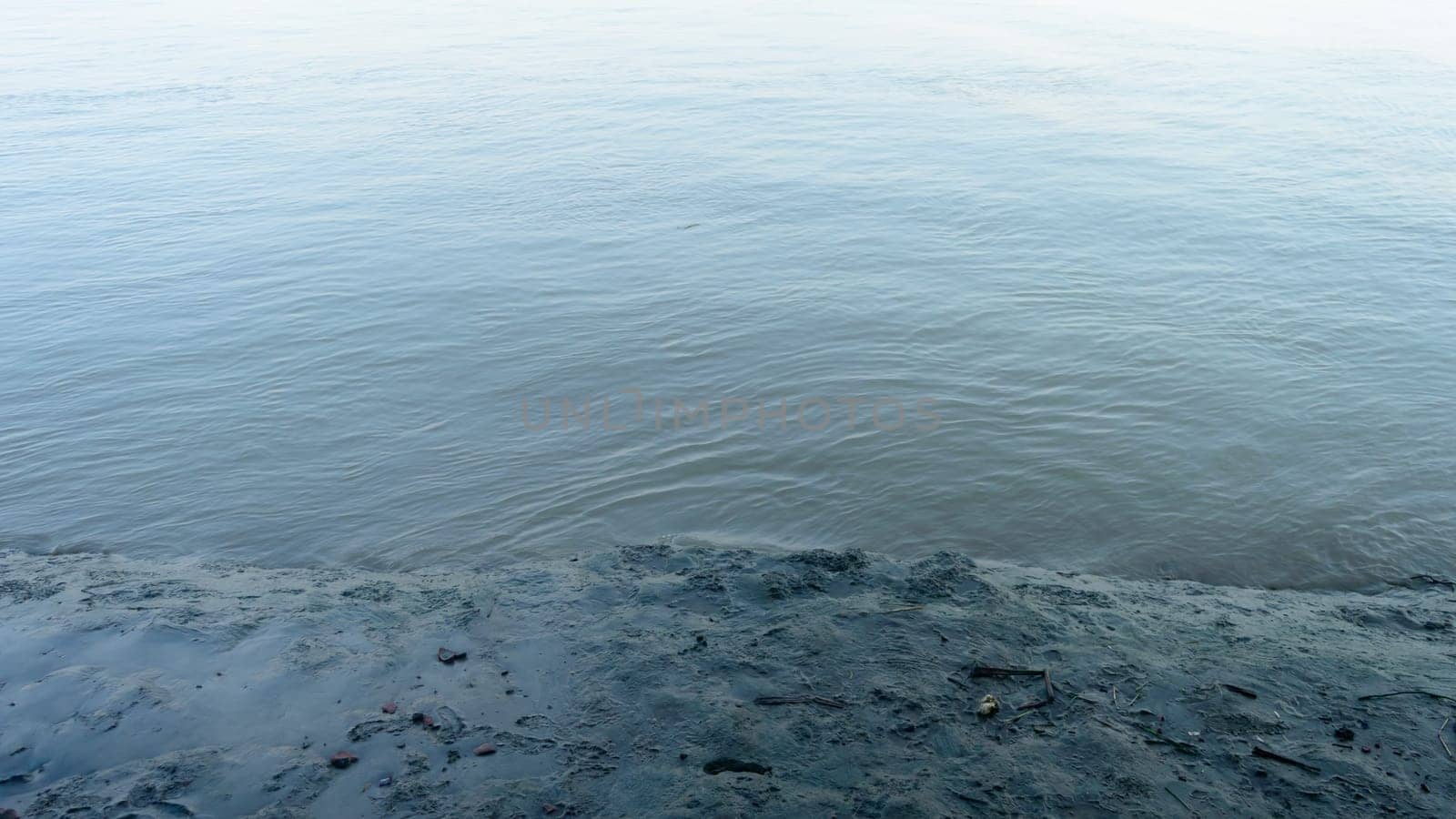 Muddy river banks in low tide next to wave water. Alluvial soils deposited by the river. Nature background. Close up.