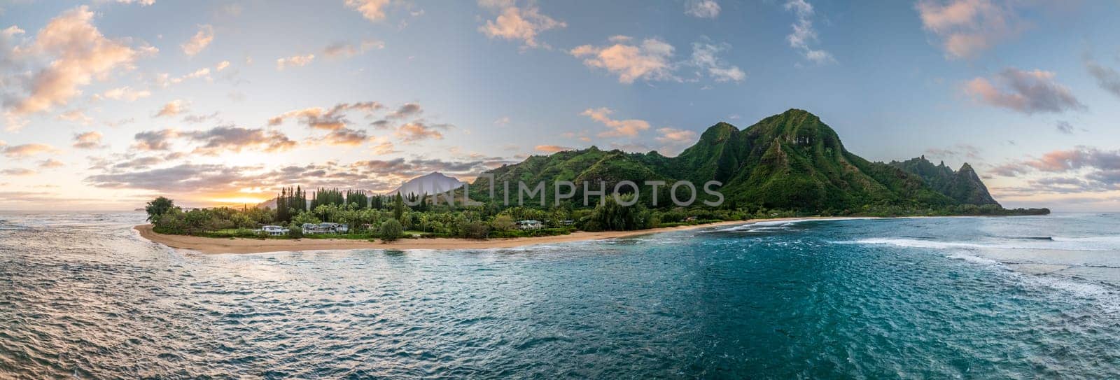 Tunnels Beach panorama view from above at sunset, with the clear turquoise water and lush green mountains in the background