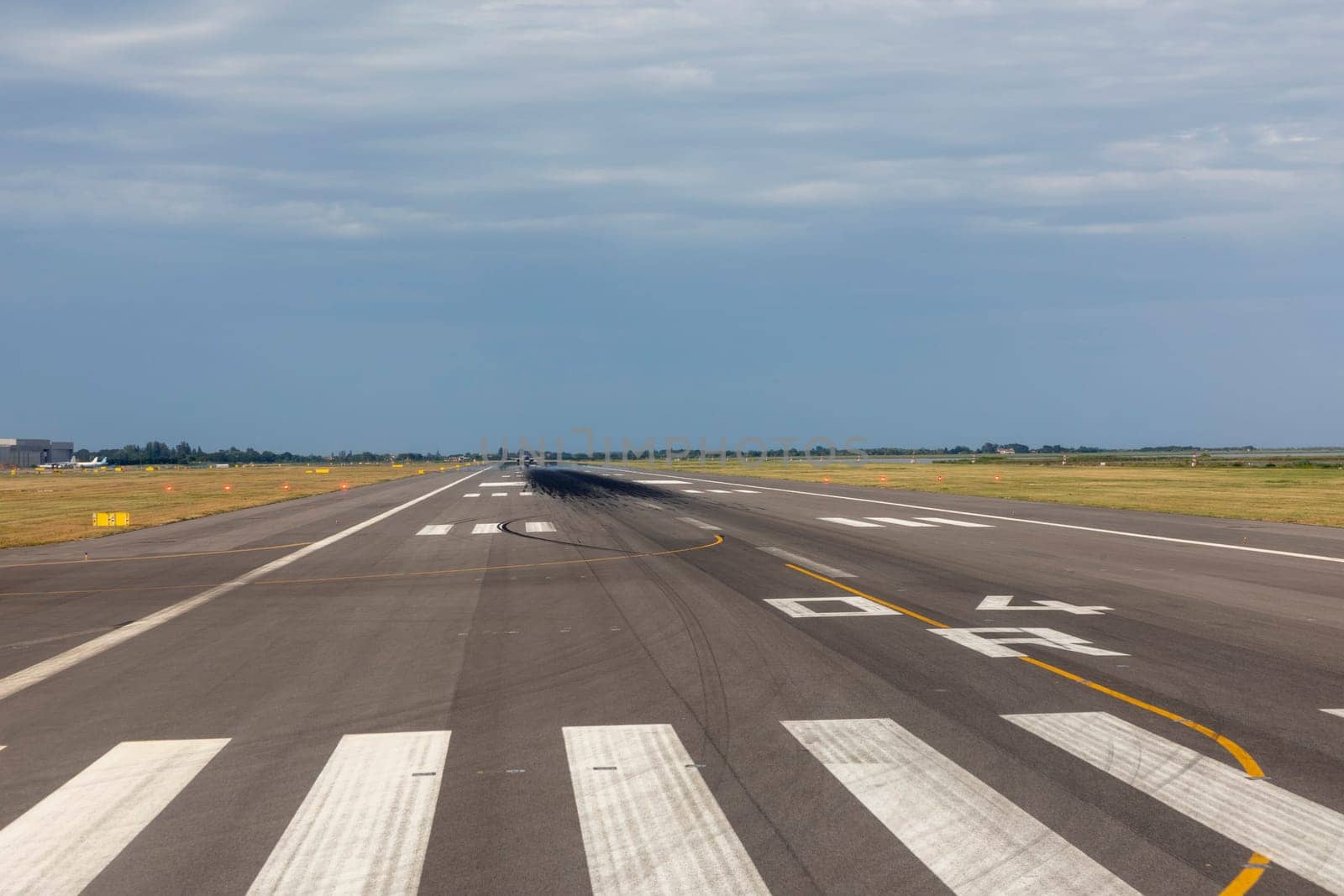 runway of airport with cloudy sky and print of wheels at the surface
